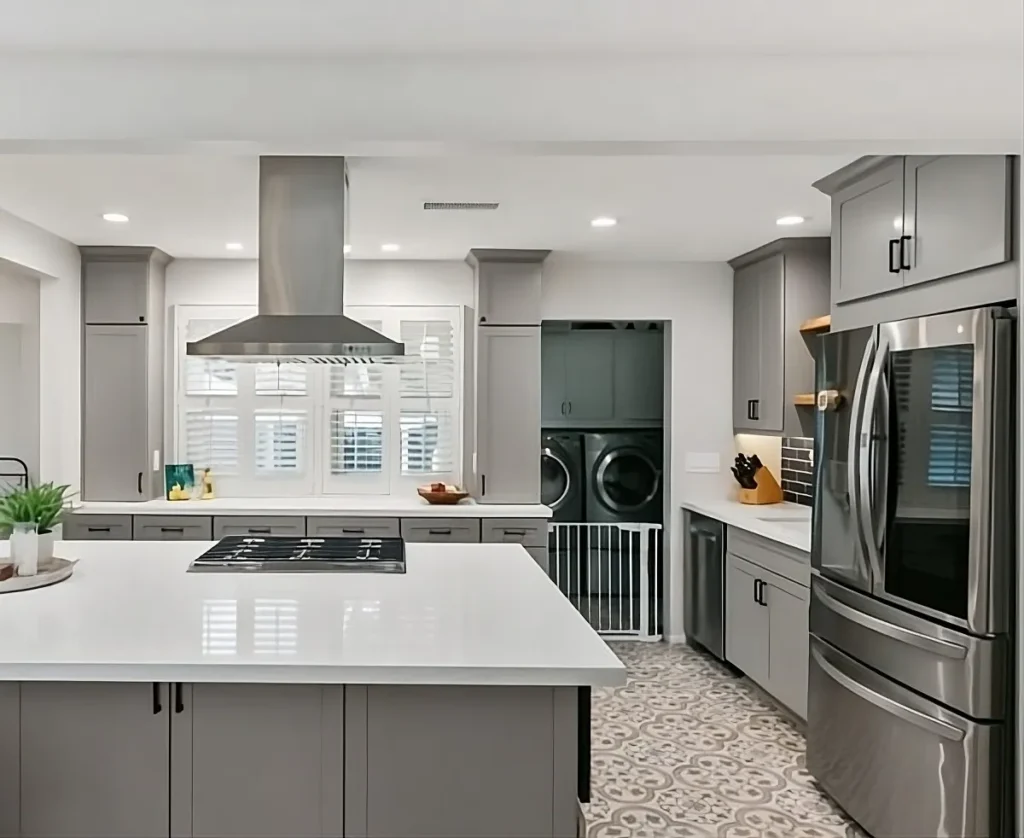Modern kitchen with large island, gray shaker cabinets, patterned tile flooring, and a view into the adjacent laundry room.
