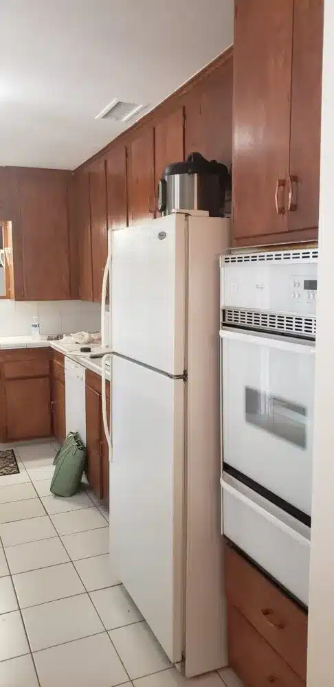 A dated kitchen with dark wood cabinets, white appliances, and a narrow galley layout.