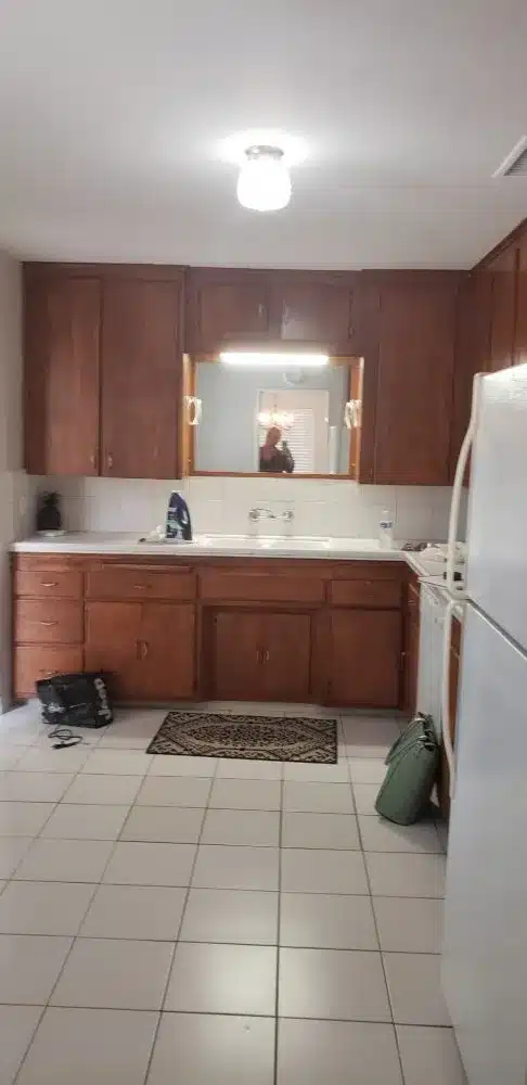 Old kitchen with dark cabinets, white tile floors, and a mirror above the sink area.