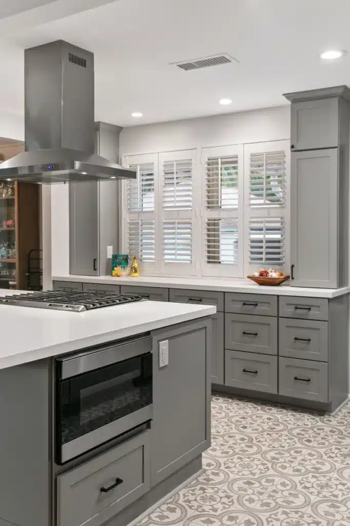 Kitchen island with built-in microwave, gas cooktop, patterned tile floor, and white shuttered windows in the background.