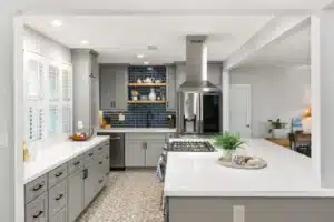 Open concept kitchen remodel featuring gray Mantra cabinets, a large island with gas cooktop, and a navy subway tile backsplash.